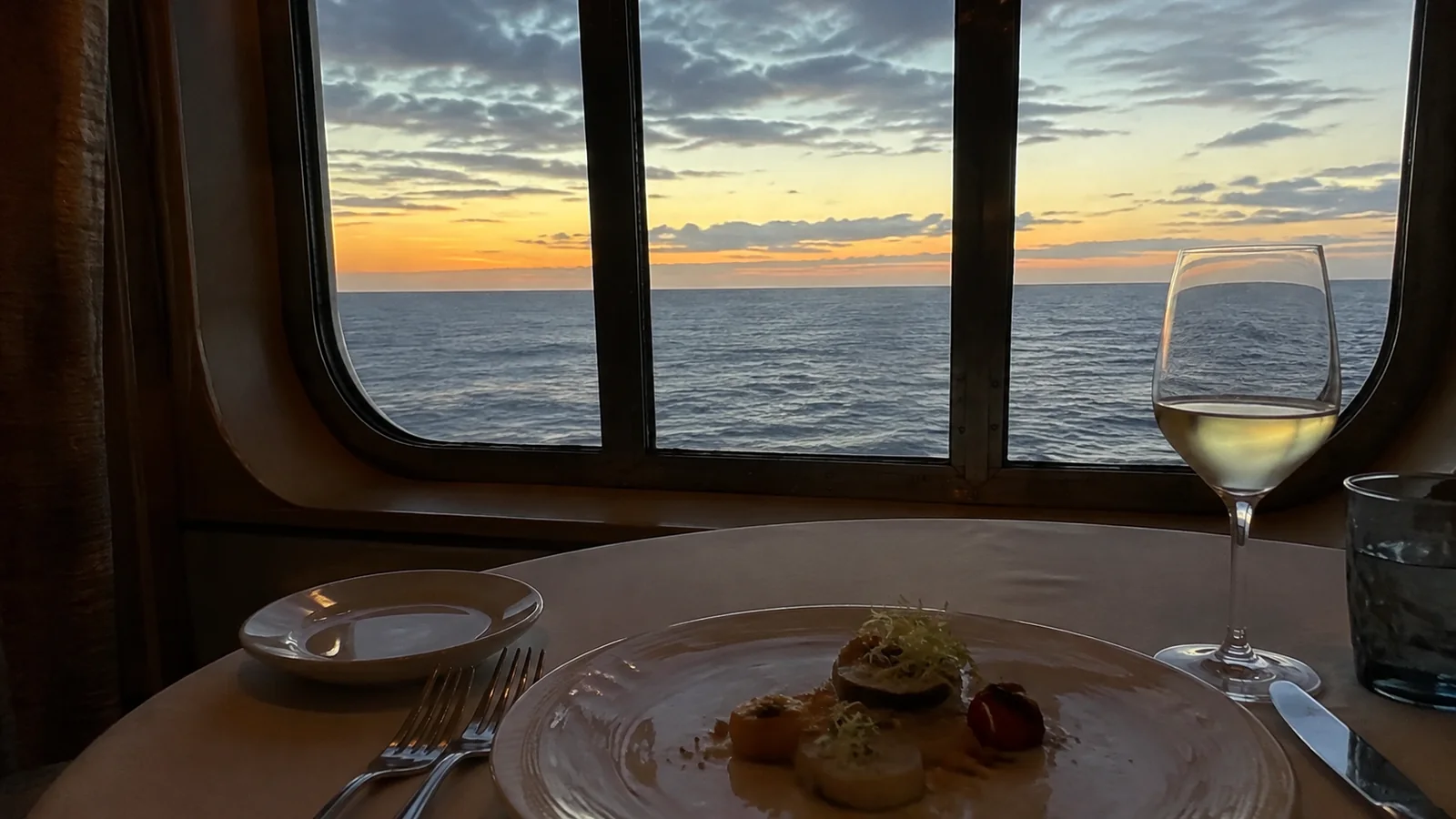 Dinner plate and wine glass sit beside a window at sunset.