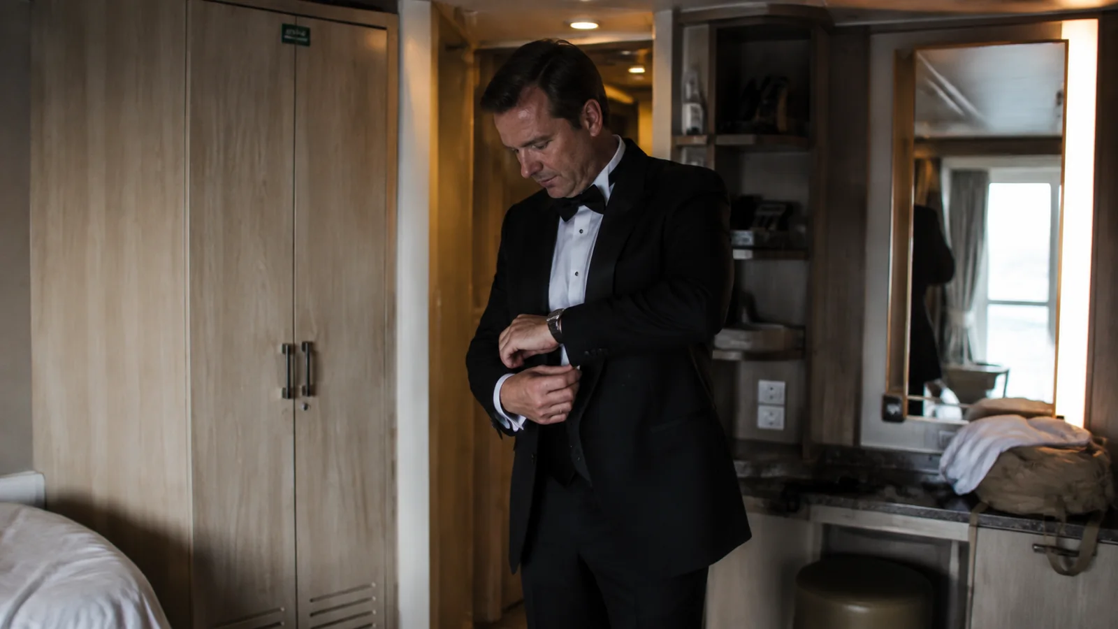 Man adjusts his formal jacket inside a cruise stateroom.