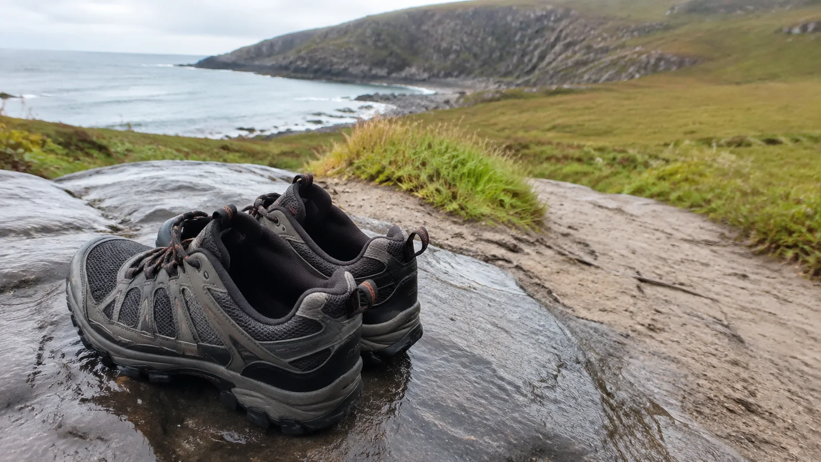 Hiking shoes rest on a broad rock above the coast.