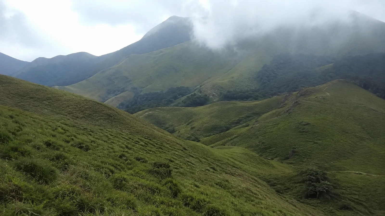 Mist hangs over rolling green mountains and steep grassy valleys.
