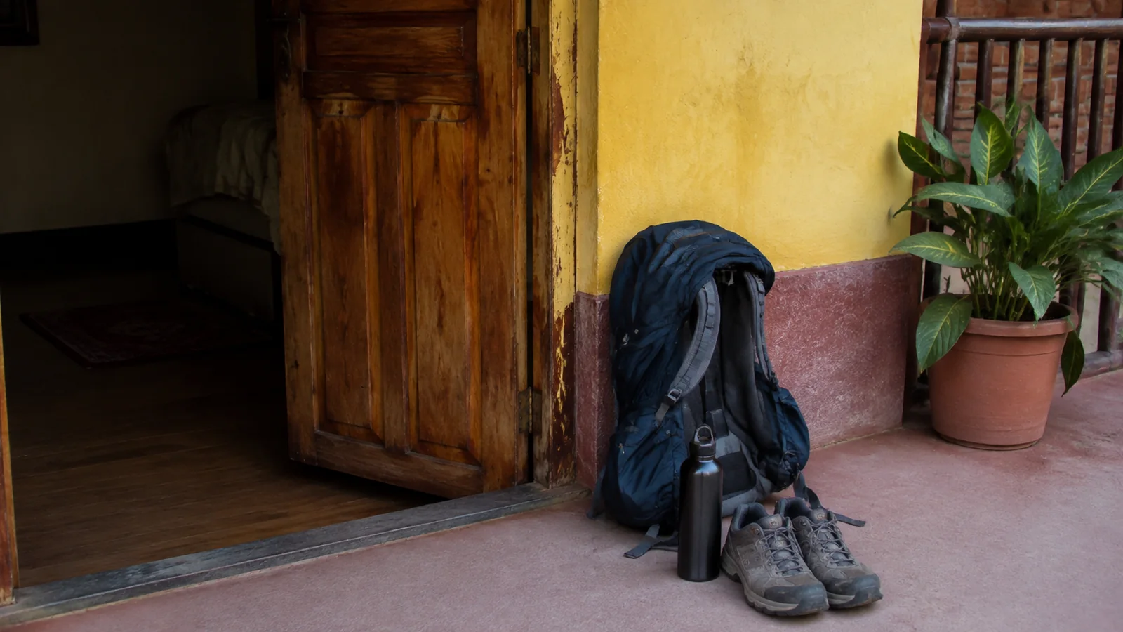 Backpack, shoes, and reusable bottle rest outside a guesthouse doorway.