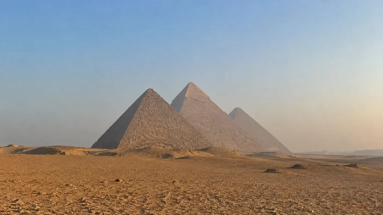 Three pyramids rise above a sandy desert plain.
