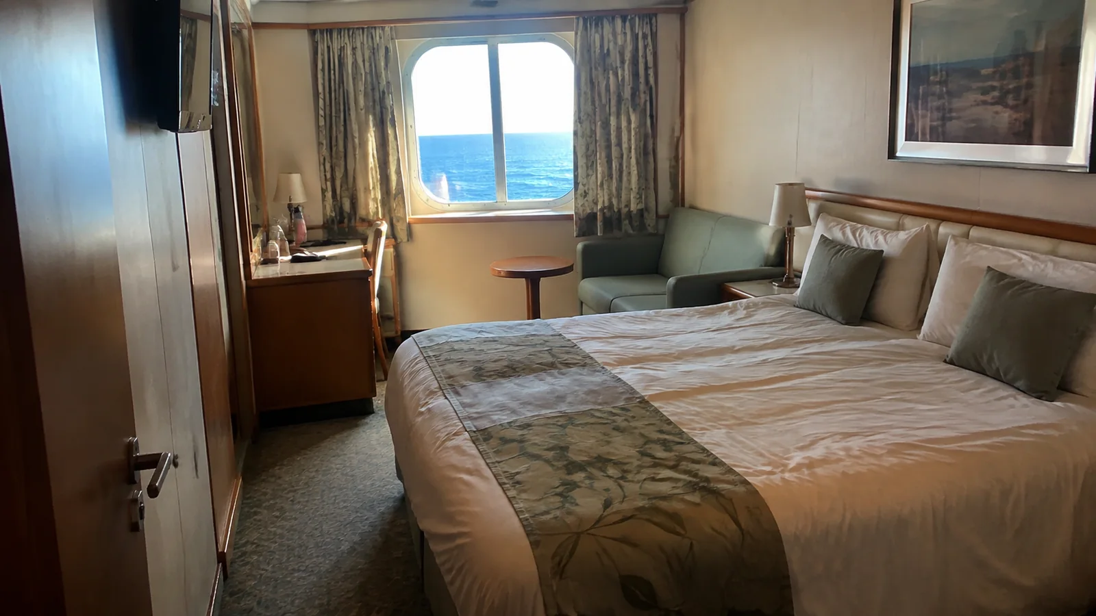 Ocean-view cabin with a double bed, desk and small sofa.