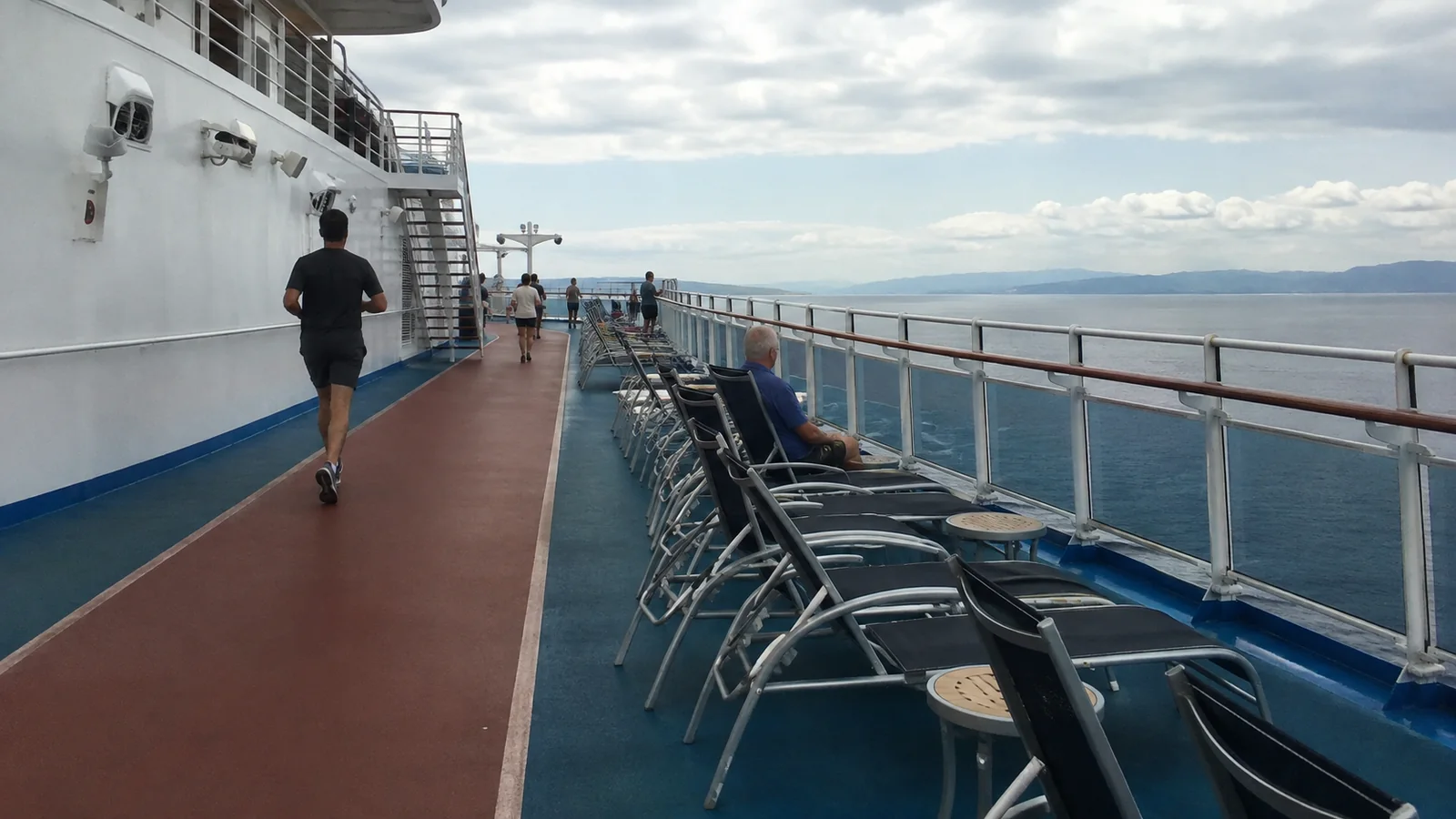 Jogger on a ship's outdoor track beside rows of deck chairs.