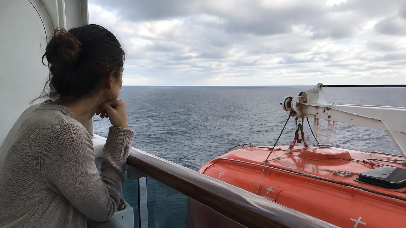 Passenger leaning on a railing above a lifeboat and its davit.