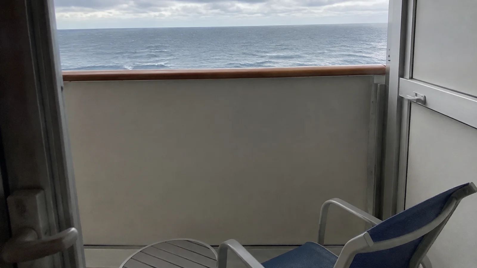 Small balcony with a solid lower railing and folding chair.