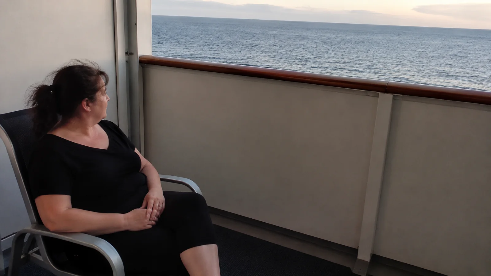 Passenger relaxing on a partially enclosed balcony at sunset.