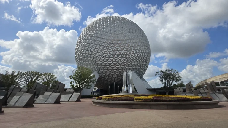 Large silver geodesic sphere above landscaped grounds beneath scattered clouds.