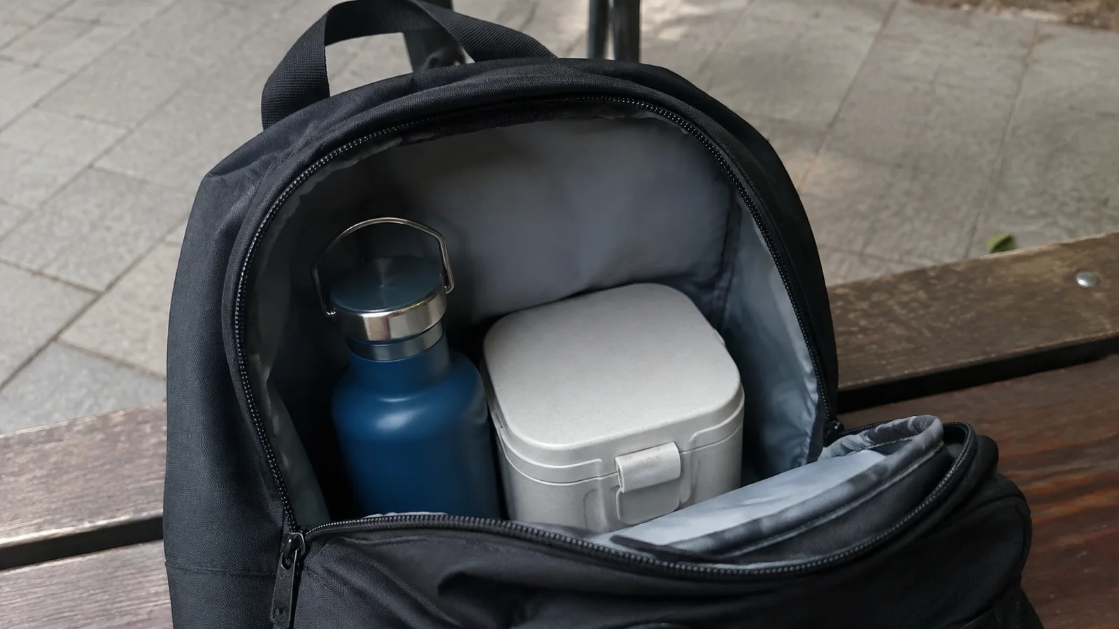 Reusable water bottle and food container packed inside an open backpack.