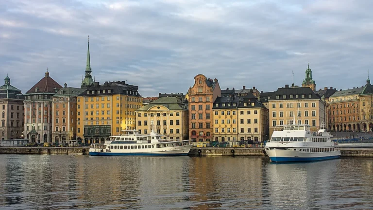 Historic waterfront buildings with pointed church spires and moored passenger boats.