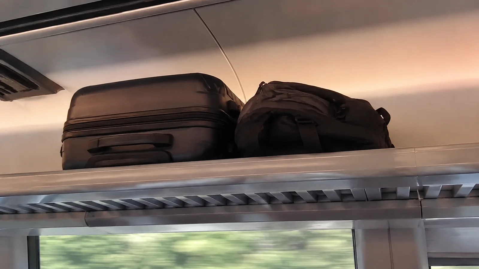Suitcase and backpack stored on an overhead train luggage rack.