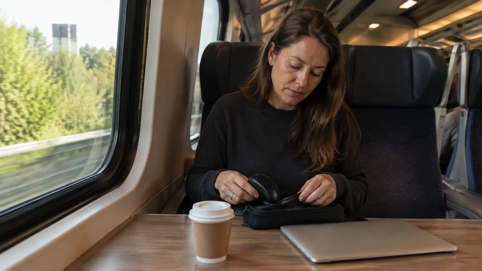 Passenger arranging belongings at a train table beside a window.
