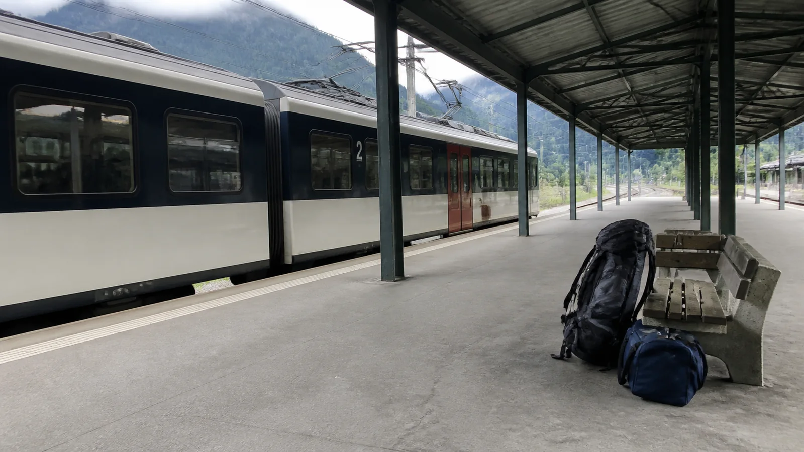 Backpack and small bag rest beside a train on a covered station platform.