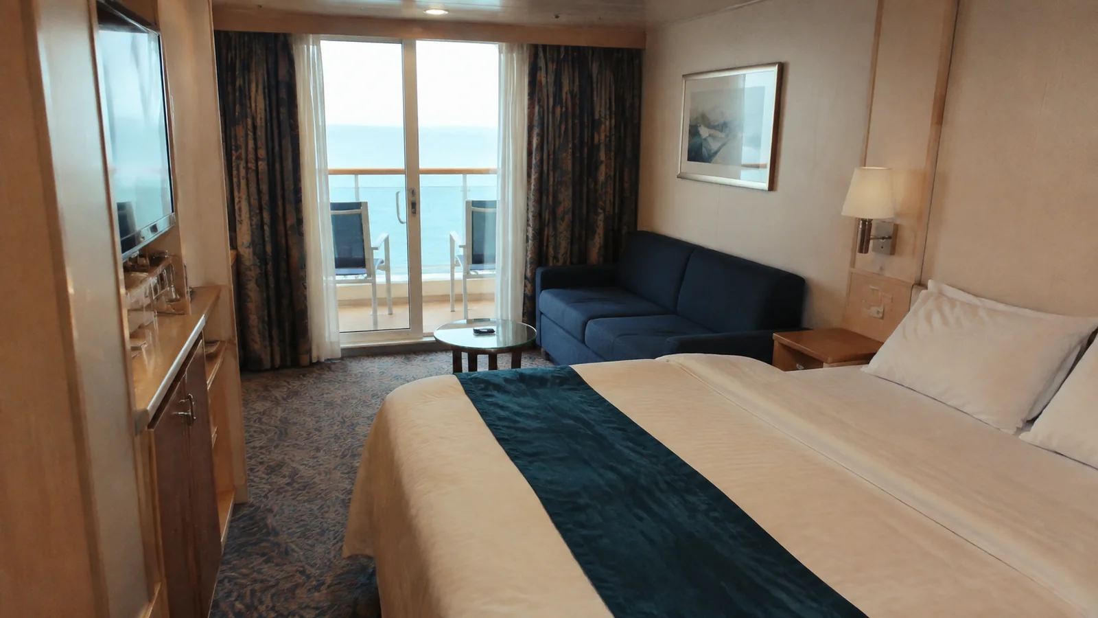 Ship cabin with a double bed, blue sofa, and balcony doors.
