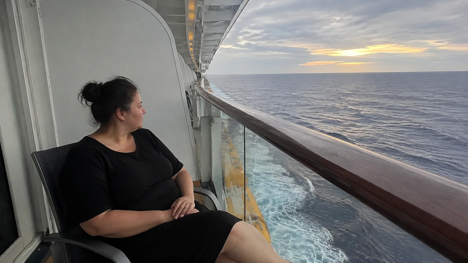 Woman seated on a ship balcony watching the sunset over the ocean.