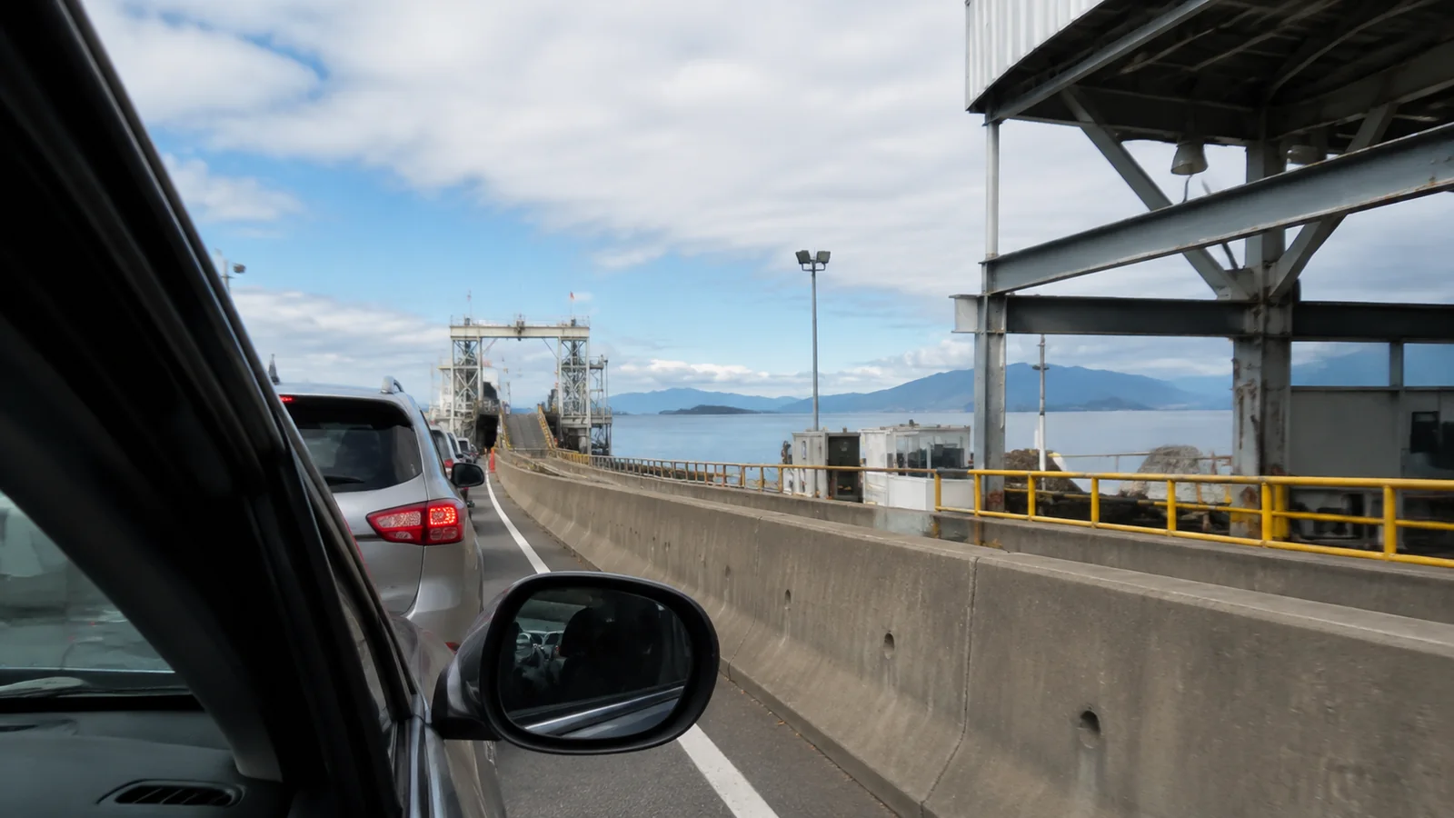 Cars waiting in a ferry loading lane beside open water.