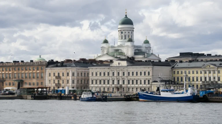 White domed cathedral rises above waterfront buildings and moored boats.