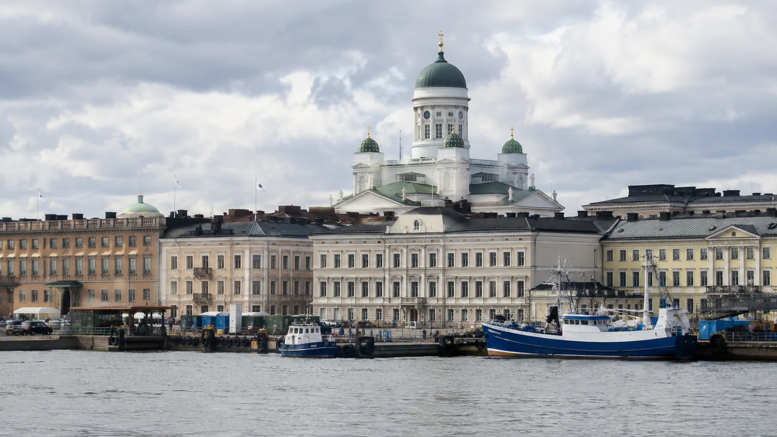White domed cathedral rises above waterfront buildings and moored boats.