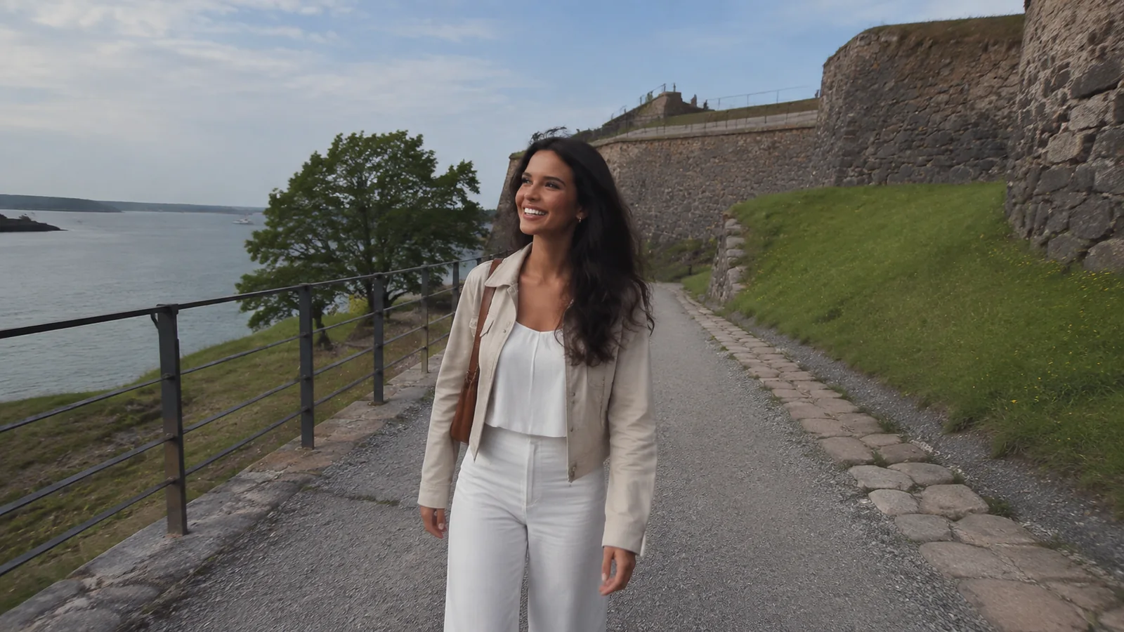 Woman walking a gravel waterfront path beside a stone fortification.