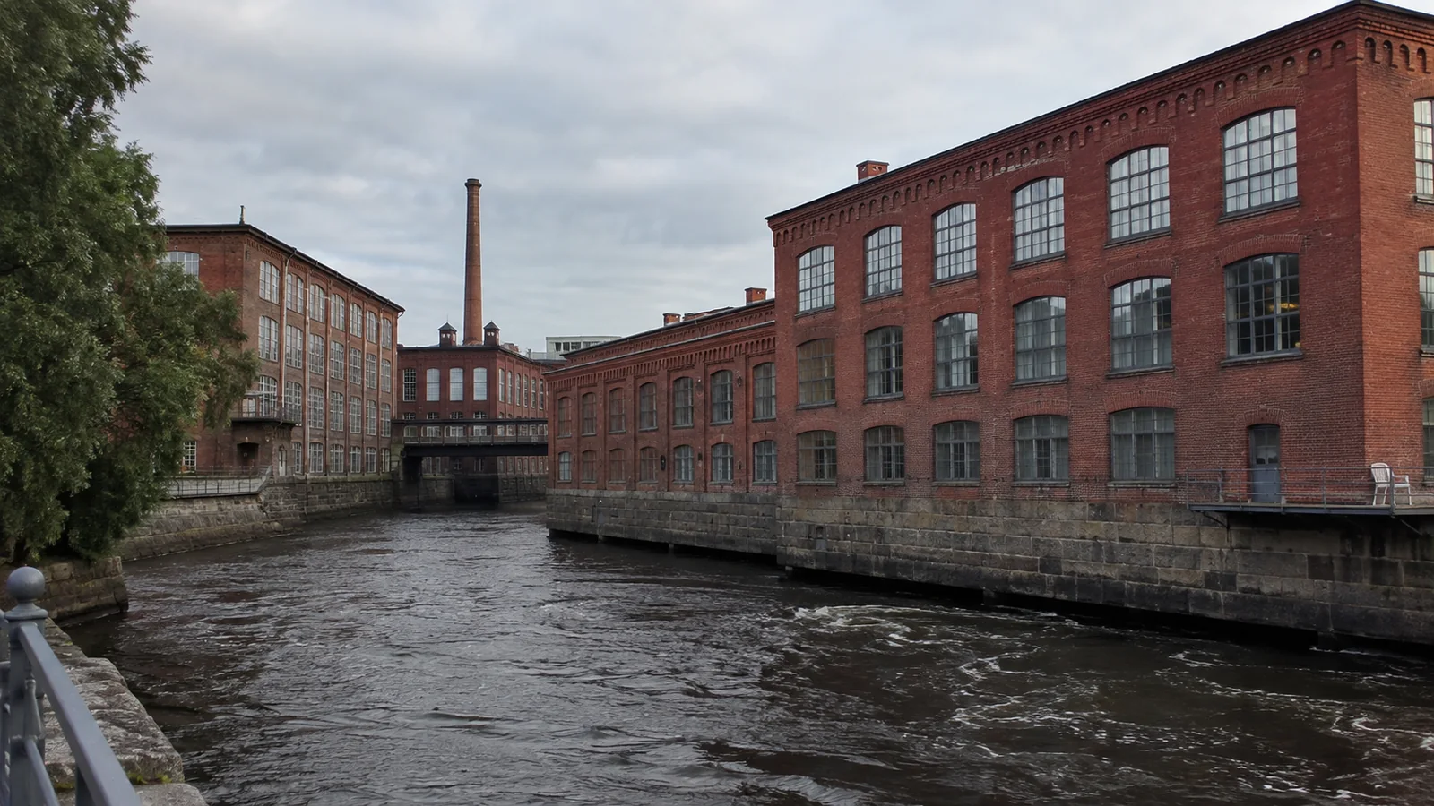 Red brick industrial buildings line a narrow flowing canal.