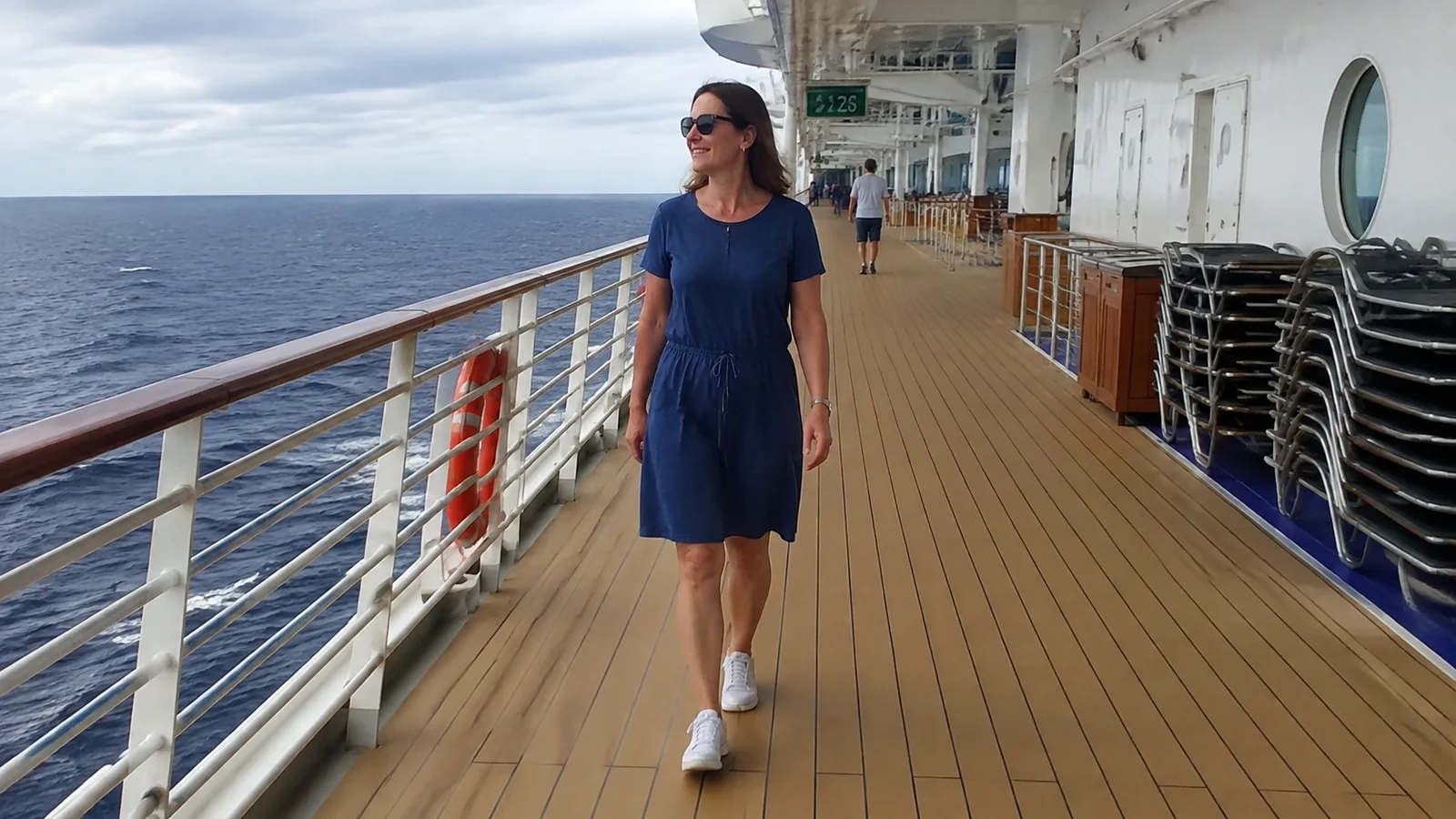Woman wearing a blue dress and sneakers on a ship's promenade.