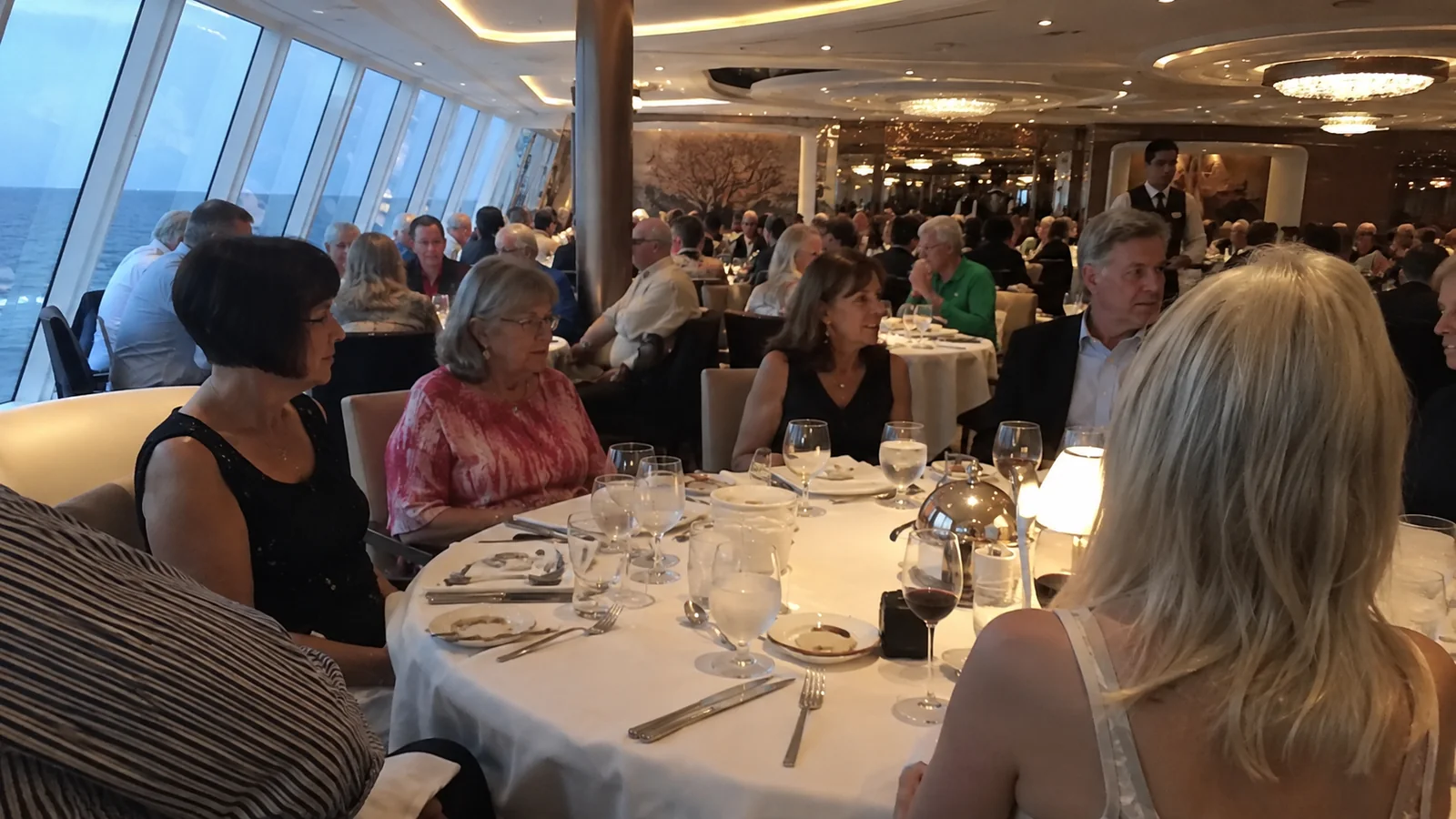 Cruise passengers in evening clothes seated around a formal dining table.