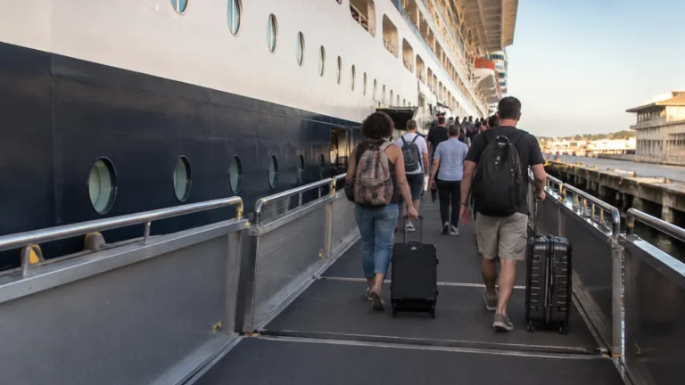 Passengers wheeling luggage up a cruise ship boarding ramp.