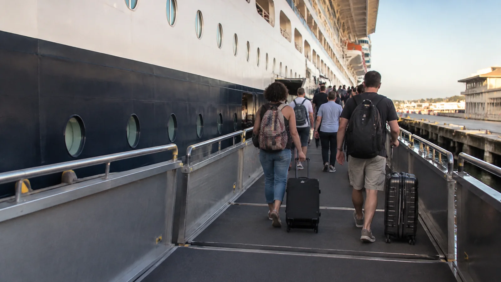 Passengers wheeling luggage up a cruise ship boarding ramp.