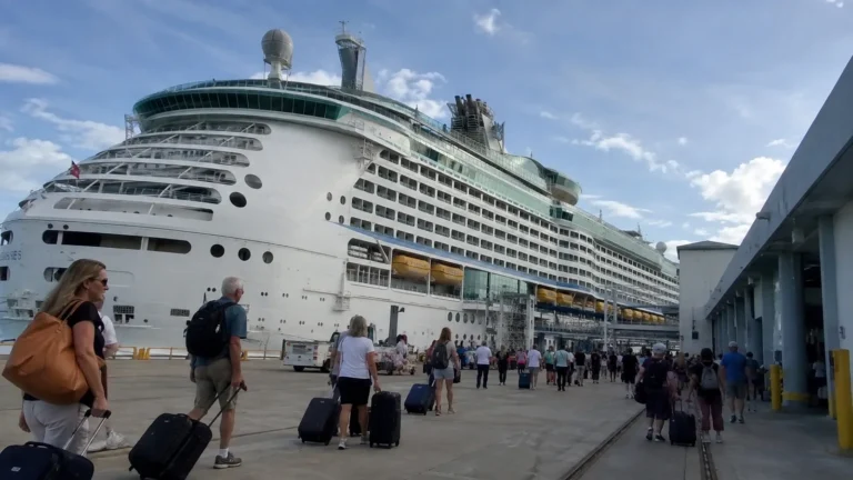 Cruise passengers arriving with luggage beside a large docked ship.
