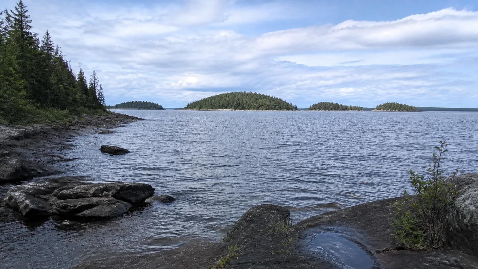 Low wooded islands lie beyond a rocky lakeshore.