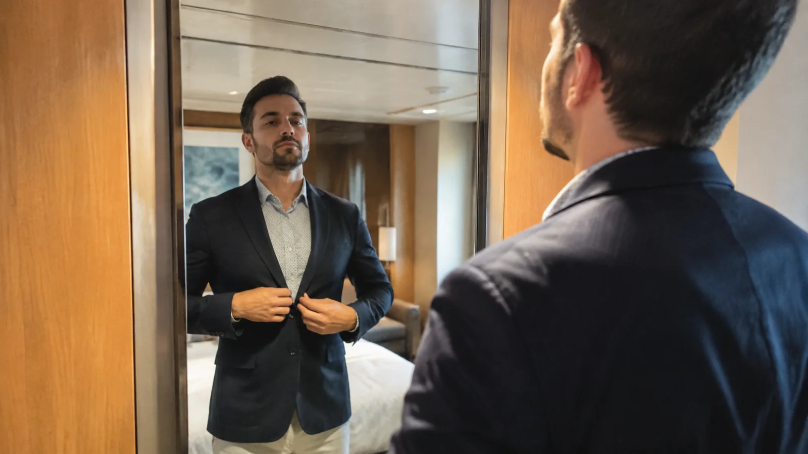 Man adjusting his blazer in a cruise cabin mirror