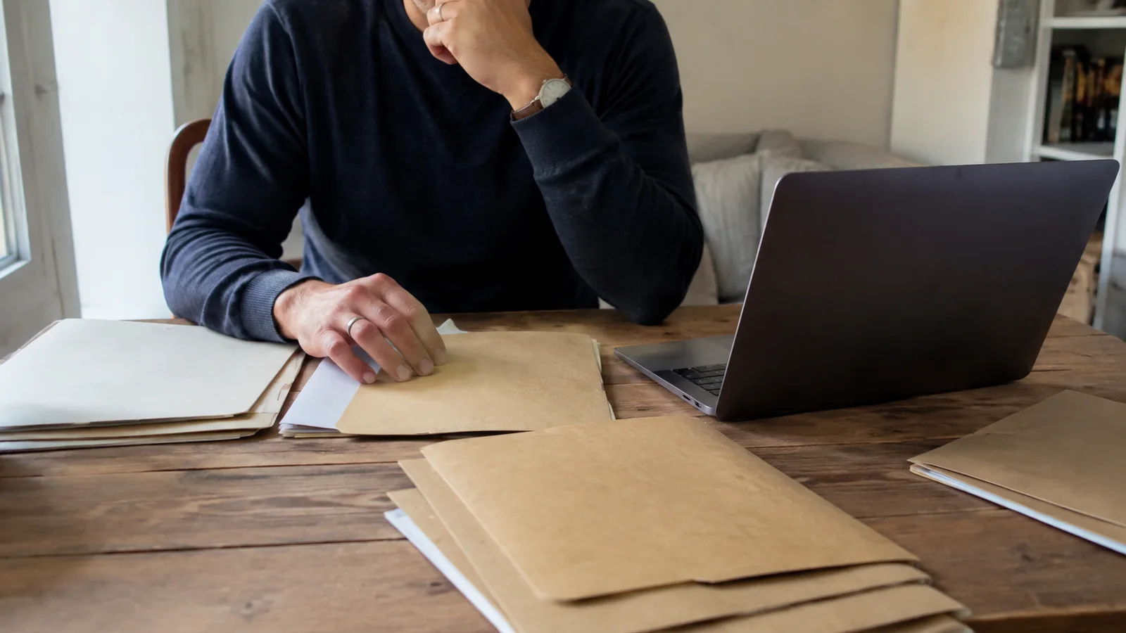 Person reviewing folders and documents at a table beside a laptop