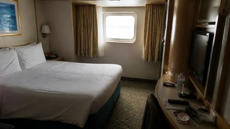 Cruise cabin with a double bed, television, and curtained window