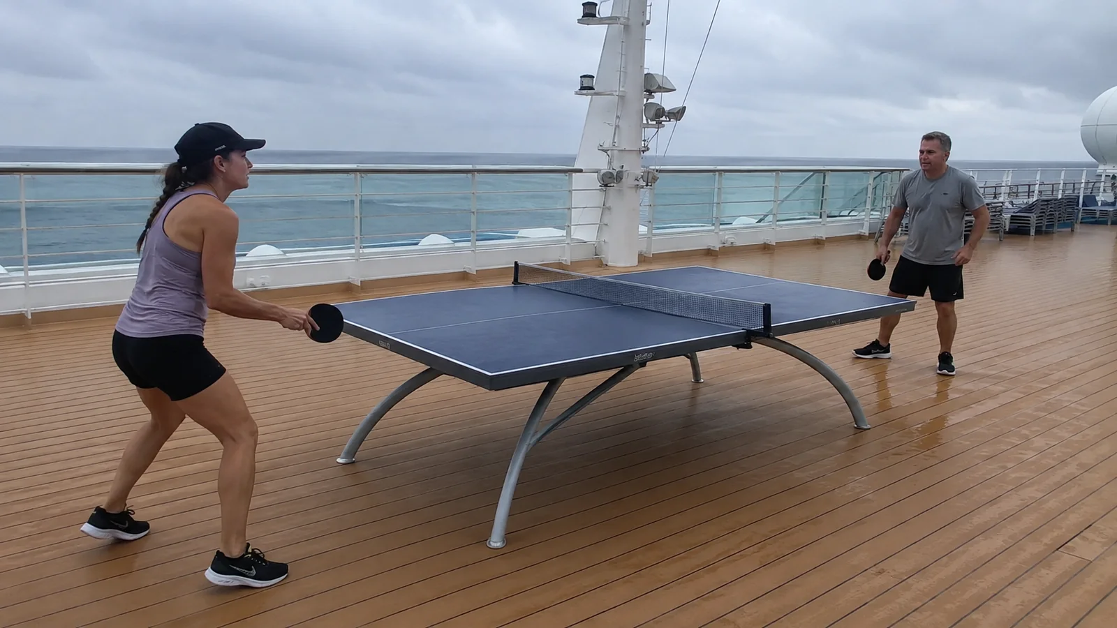 Two passengers play table tennis on an outdoor ship deck.