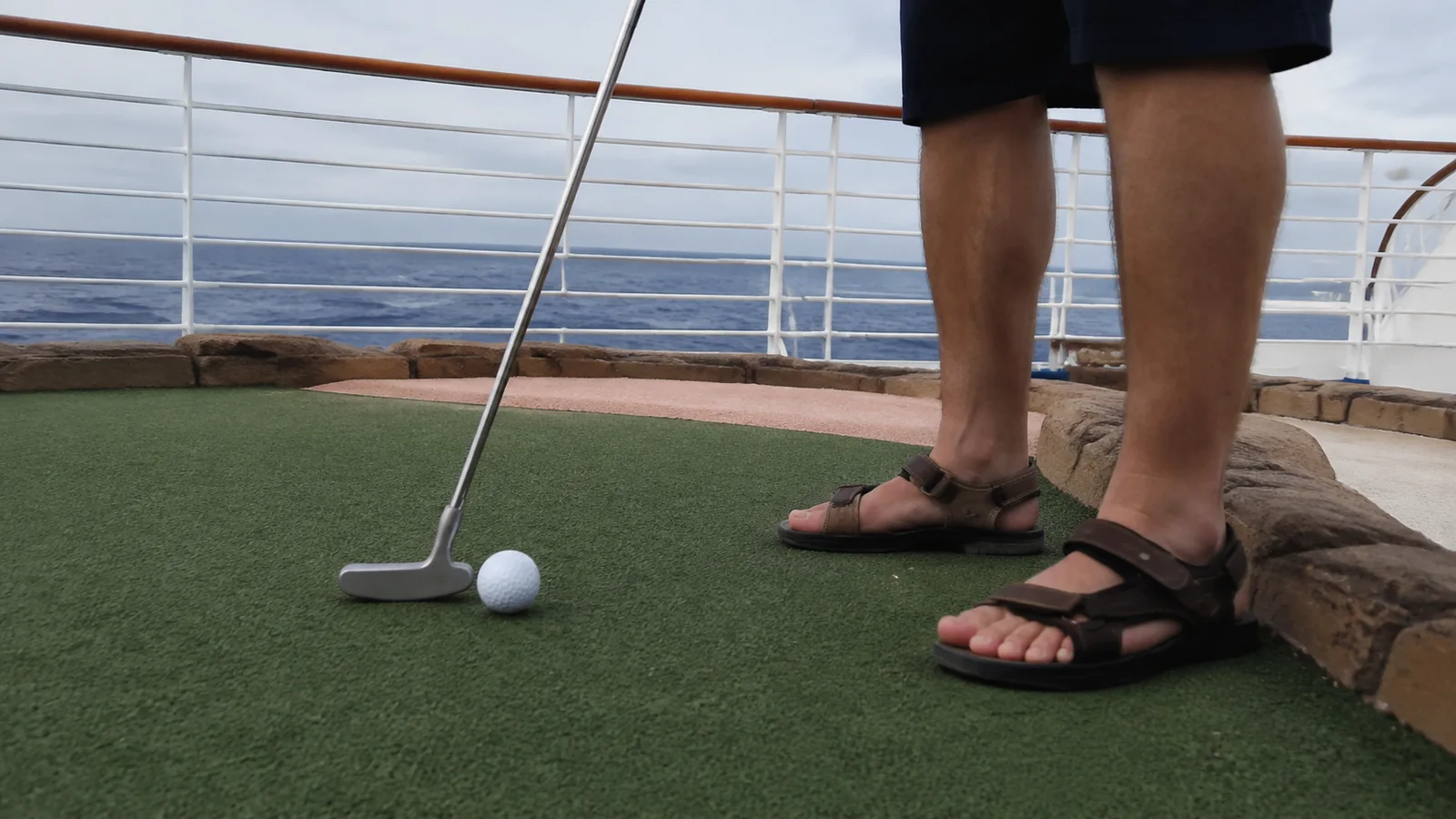 Close view of a putter and golf ball on a miniature golf course.