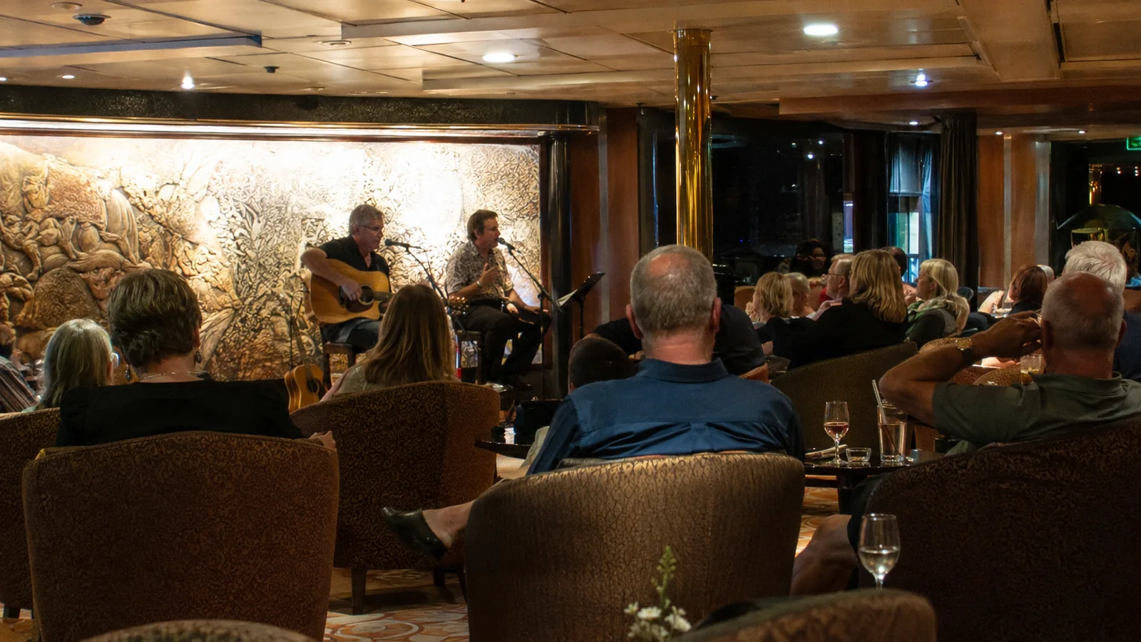 Passengers watch acoustic musicians perform in a warmly lit lounge.