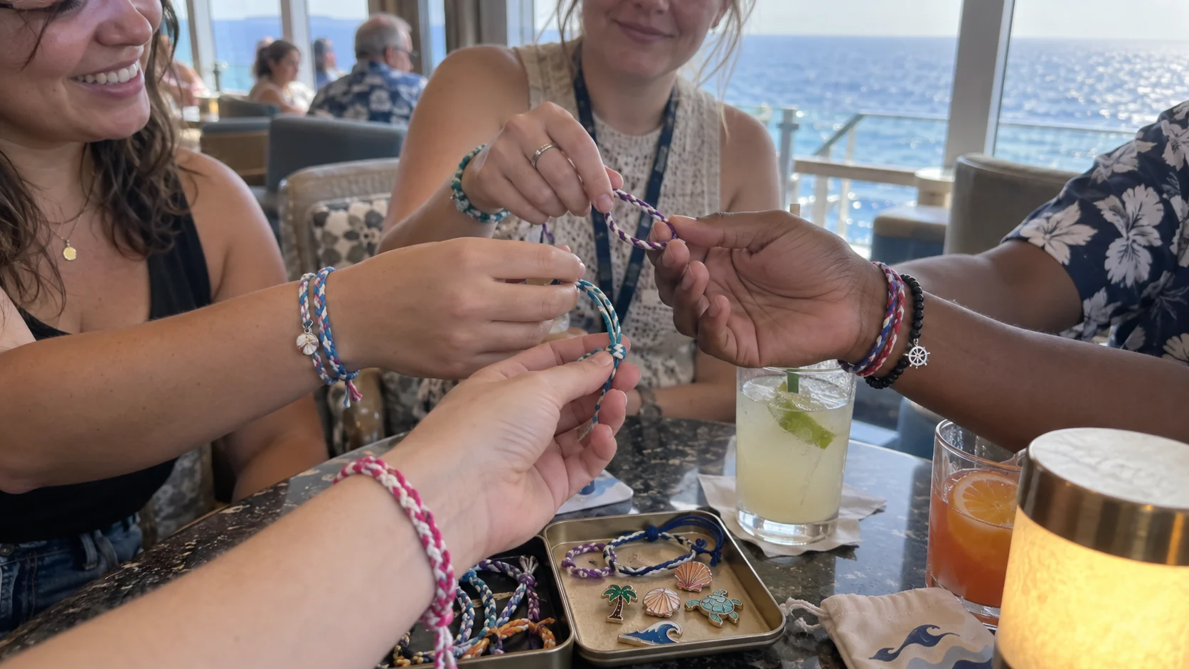 Friends exchanging handmade friendship bracelets around a cruise ship lounge table.
