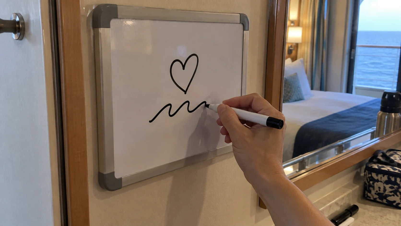 Hand drawing a heart and wave on a private magnetic message board in a cruise cabin.