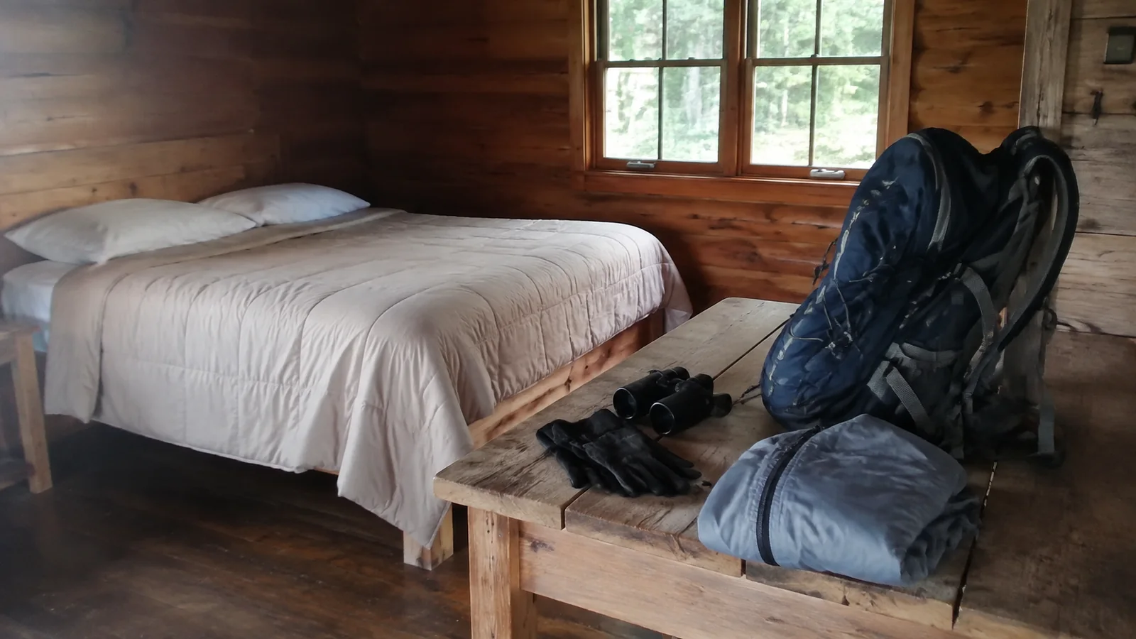 Backpack and outdoor gear arranged beside a bed in a wooden cabin.