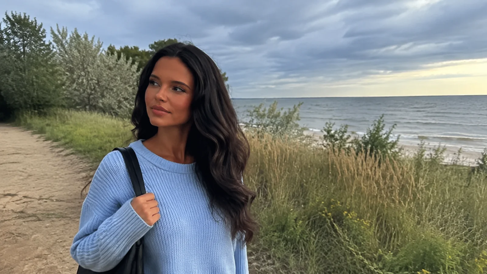Woman walking a grassy beach path with a bag over her shoulder.