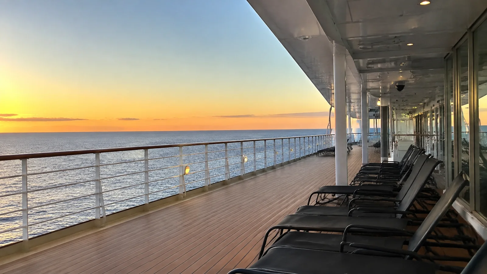 Empty loungers line a ship's covered promenade at sunset.