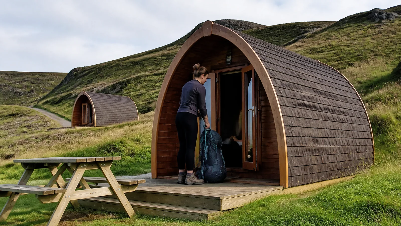Traveler carrying a bag into an arched wooden camping cabin.