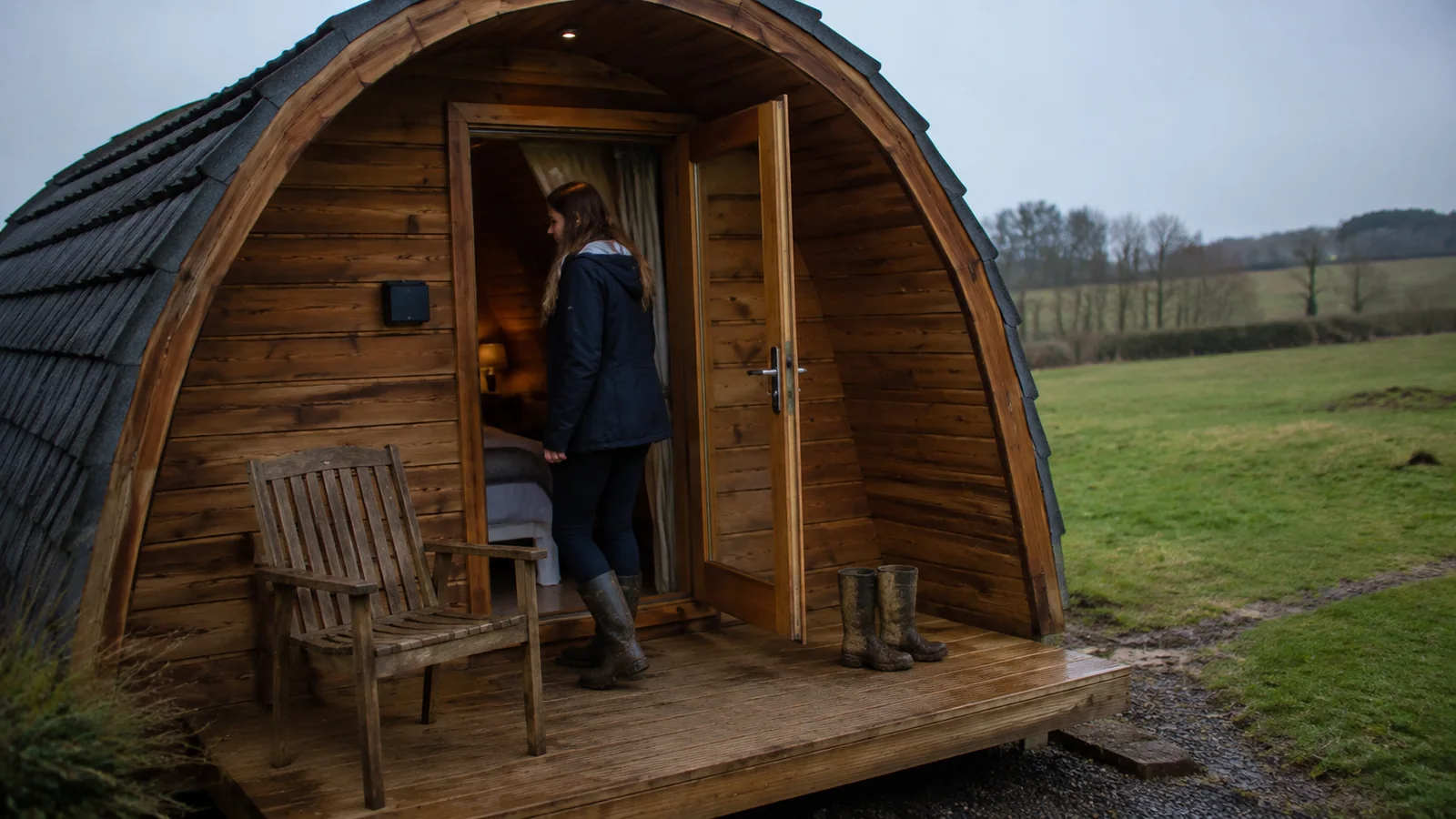 Woman standing in the doorway of a wooden camping cabin beside boots.