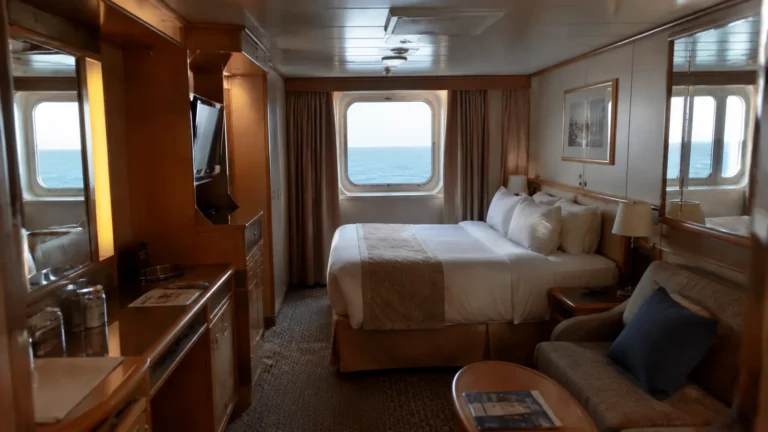 Ocean-view cruise cabin with a double bed, sofa and wooden furnishings.