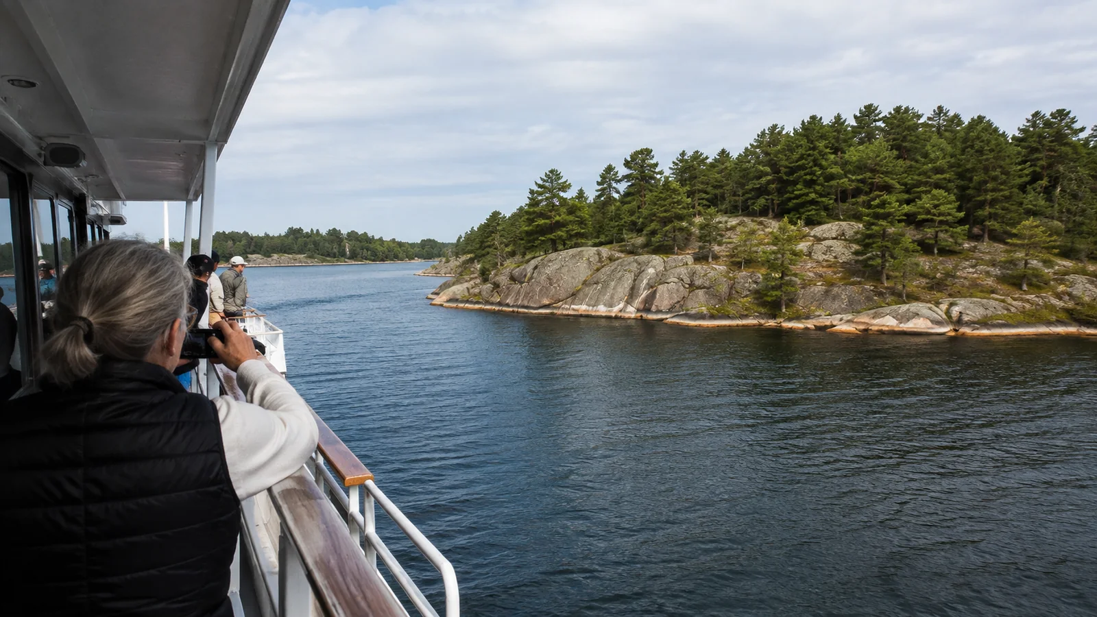 Passengers photographing a rocky, pine-covered island from a ship.
