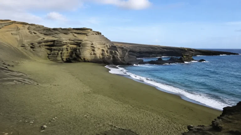 Green sand beach curves beneath layered cliffs beside blue ocean water.