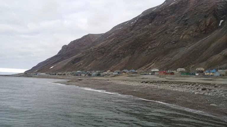 Small coastal settlement beneath a steep barren mountain beside calm water.