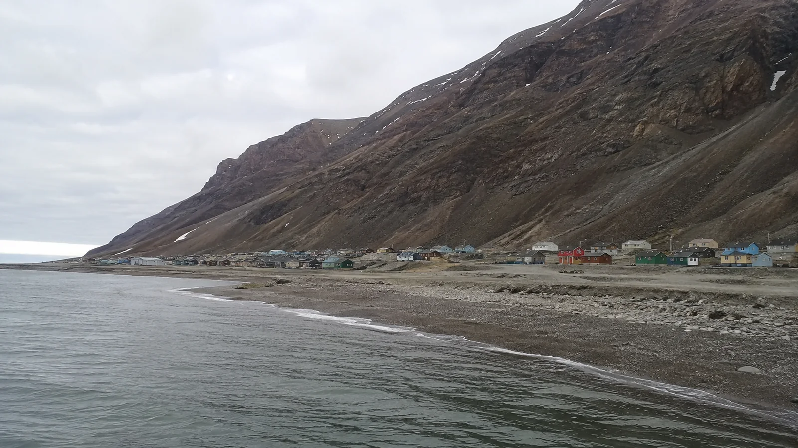 Small coastal settlement beneath a steep barren mountain beside calm water.
