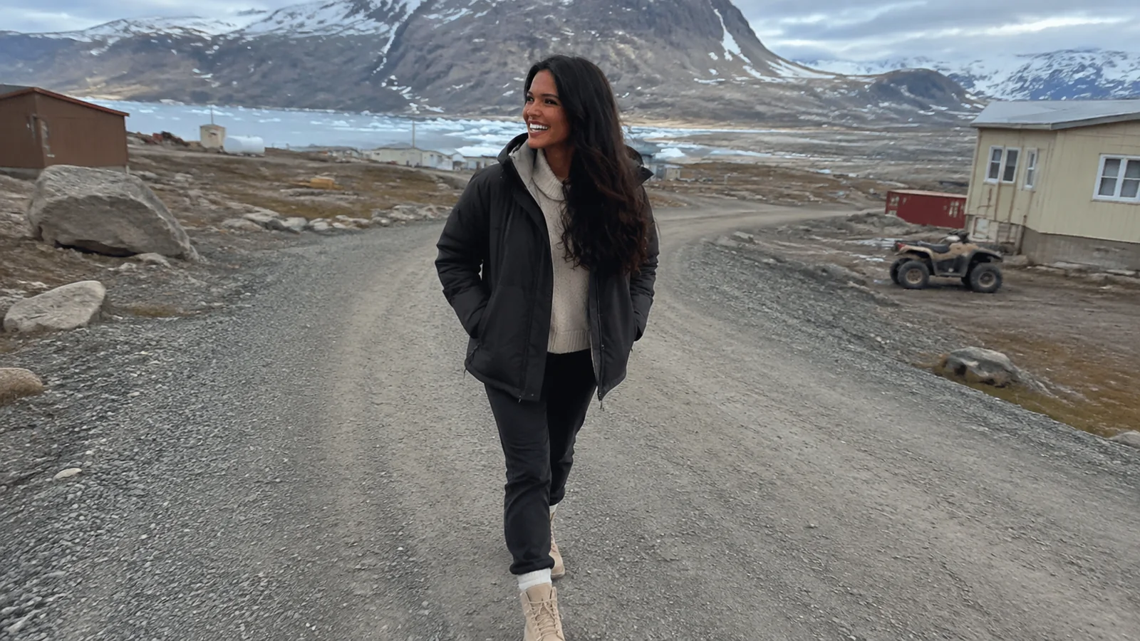 Woman walking a gravel village road with snowy mountains behind.