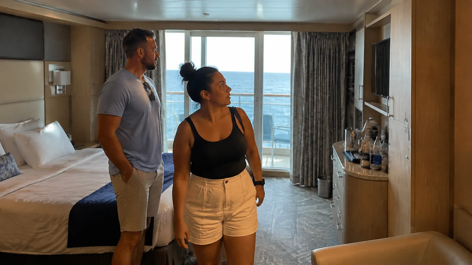 Couple stands inside a balcony stateroom looking around the room.